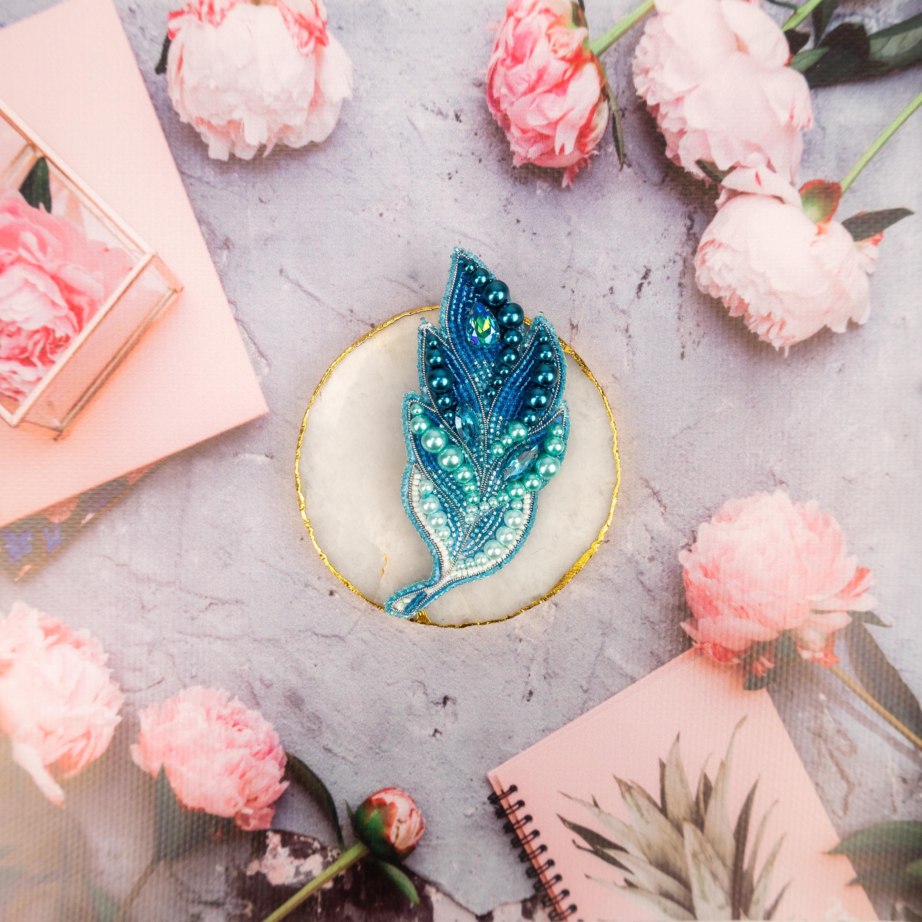 a blue brooch sitting on top of a table next to pink flowers